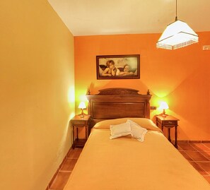 A hotel room with a bed, two bedside tables with lamps, a wooden headboard, and a painting above the bed. - Traditional Andalusian Mansion, Cordoba (Moriles)