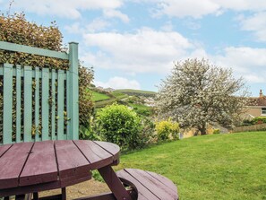 A wooden picnic table in a grassy yard with a view of houses and hills in the background. - Quay Sands, Hope Cove (Kingsbridge)