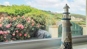 A coastal view with a stone lighthouse, lush greenery, and a glimpse of houses in the distance. - Quay Sands, Hope Cove (Kingsbridge)