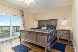 A bedroom with a large bed, a nightstand, a dresser, and a balcony with a view. - Sea Turtle - Gulf Beachfront, 5 Bedroom, 4 Bath, Sleeps up to 13 (Dauphin Island)
