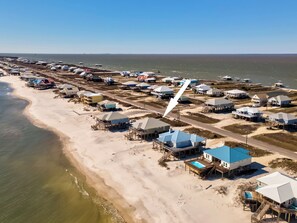 An aerial view of a coastal area with beach houses, some with elevated structures, and a clear view of the ocean. - Sea Turtle - Gulf Beachfront, 5 Bedroom, 4 Bath, Sleeps up to 13 (Dauphin Island)
