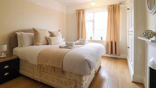 A neatly arranged bedroom with a large bed, bedside tables, a dresser, and a window with curtains.