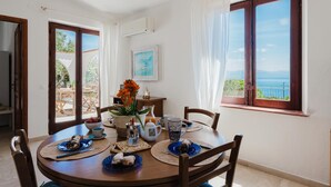 A dining area with a table set for two, a view of the sea, and a door leading to an outdoor area. - Zingaro Anima Maris, between Scopello and Zingaro (CASTELLAMMARE DEL GOLFO)