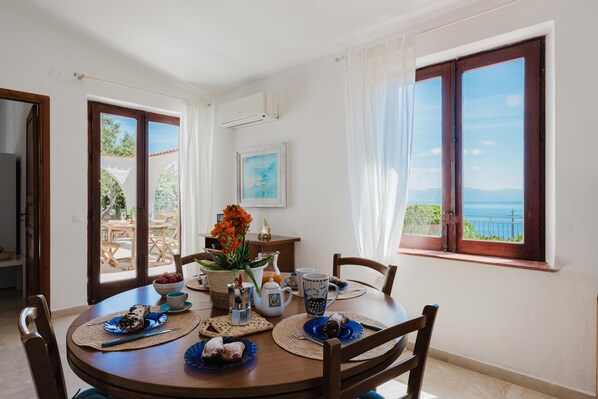 A dining area with a table set for two, a view of the sea, and a door leading to an outdoor area. - Zingaro Anima Maris, between Scopello and Zingaro (CASTELLAMMARE DEL GOLFO)