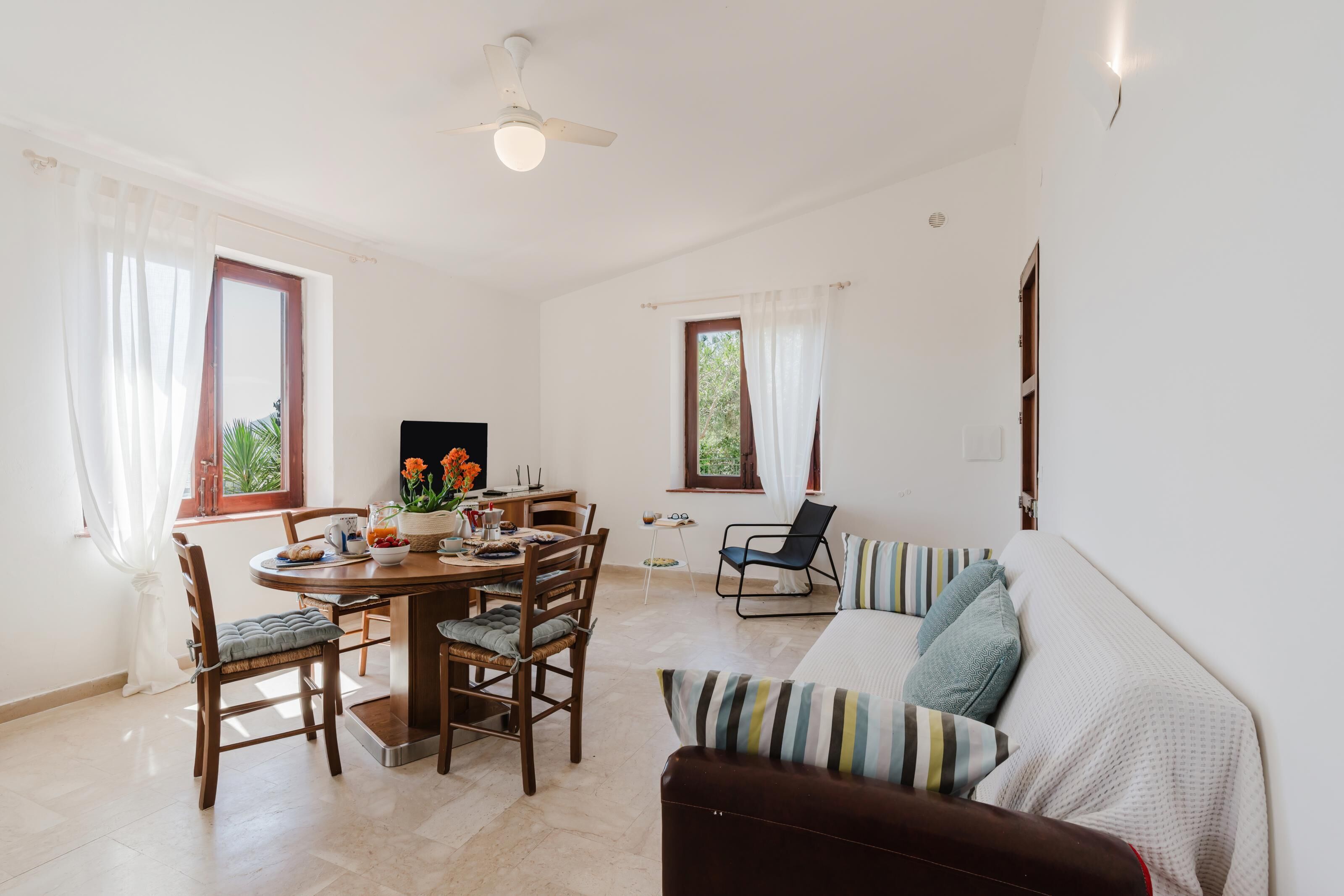 A room with a dining table, chairs, a sofa, and a TV.