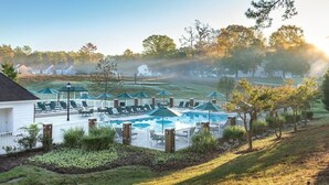 A pool area with lounge chairs and umbrellas, surrounded by a white fence and greenery. - Cozy 1 bedroom condo in Williamsburg, Virginia! (Williamsburg)