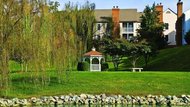 A gazebo in a grassy area with a pond, surrounded by trees and houses in the background. - Cozy 1 bedroom condo in Williamsburg, Virginia! (Williamsburg)