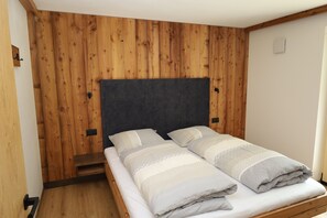 Ein Einzelbett mit Holz Kopfteil und dunkler Kopfteilverkleidung, ein kleiner Nachttisch aus Holz und eine helle Wand.