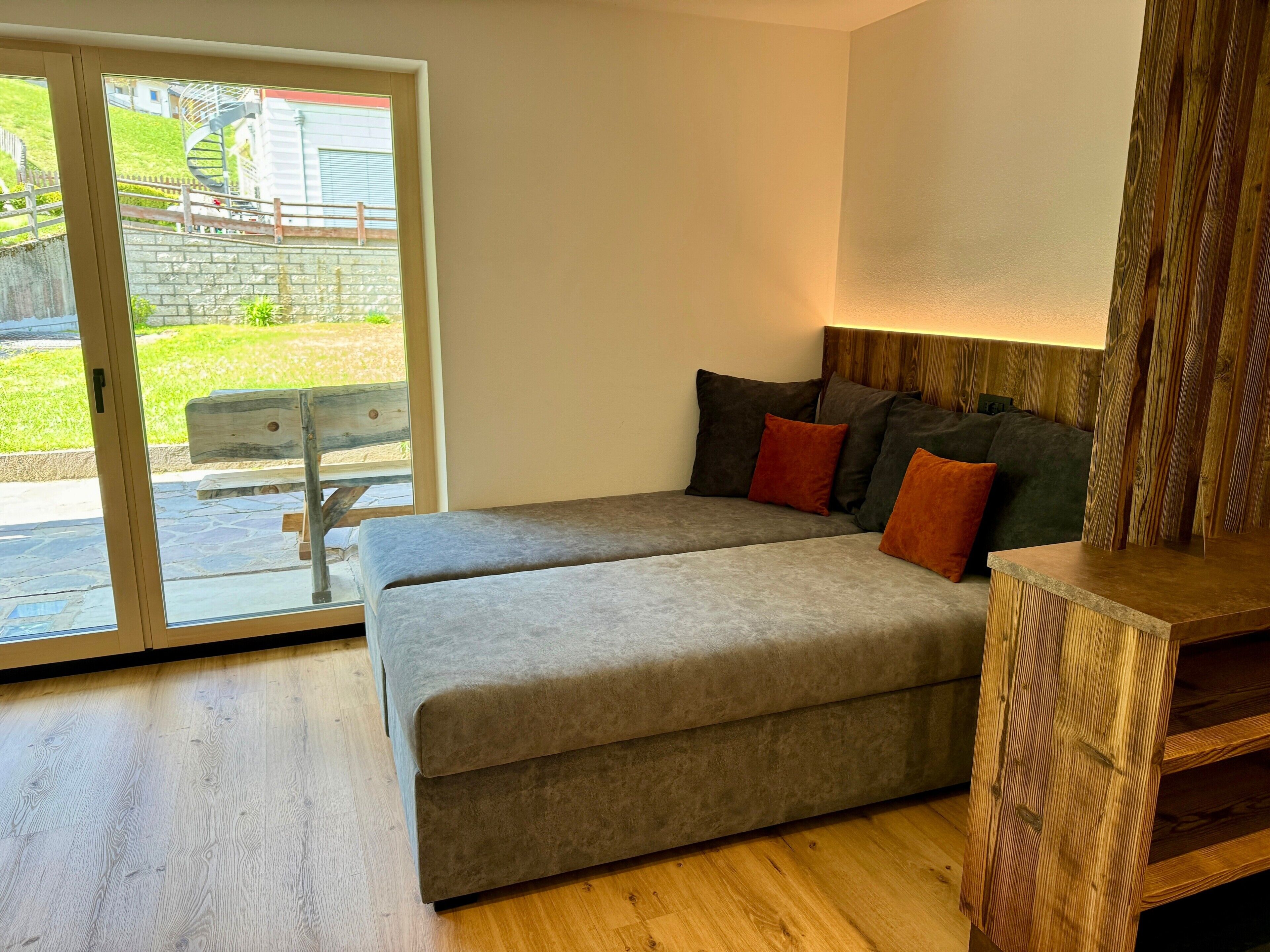 Una sala de estar moderna con un sofá gris, una mesita de madera y vistas a un espacio exterior con una escalera de caracol.