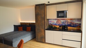 Una habitación pequeña con cama, kitchenette y un cuadro en la pared.