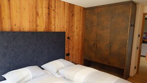 Un dormitorio con pared de madera, un armario grande y dos camas con ropa de cama estampada.