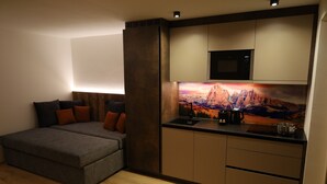 Una habitación compacta con cama, kitchenette y un cuadro grande de un paisaje montañoso.