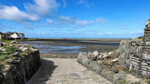 A stone pathway leading to a beach with a view of the sea and houses in the background. - Kenvor (Newport)