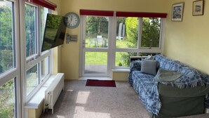A room with a sofa, a television, a clock, and a window with a view of a garden. - Kenvor (Newport)