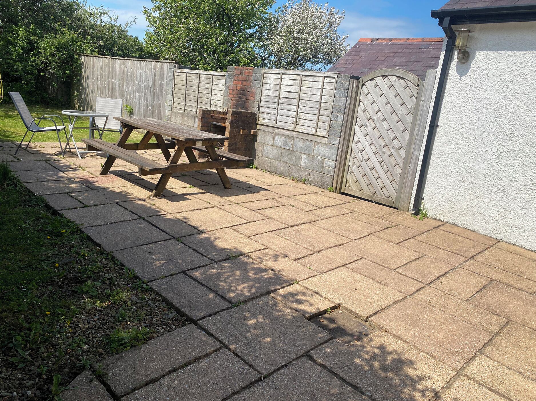 A patio with a wooden table and chairs, a brick barbecue, and a wooden fence.