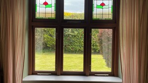 A window with three panes, each with a green and red design, overlooking a grassy area with bushes. - Kenvor (Newport)