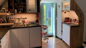 Cucina compatta con mobili bianchi, un lavello in acciaio inossidabile e diversi utensili da cucina sugli scaffali.