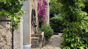 Un vialetto in pietra conduce a un edificio rustico con una porta in legno e un’ansa in metallo.
