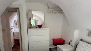 Una camera da letto con un letto, un comodino, una cassettiera e uno specchio. C'è un asciugamano rosso sul letto e un cuscino rosso sul comodino.