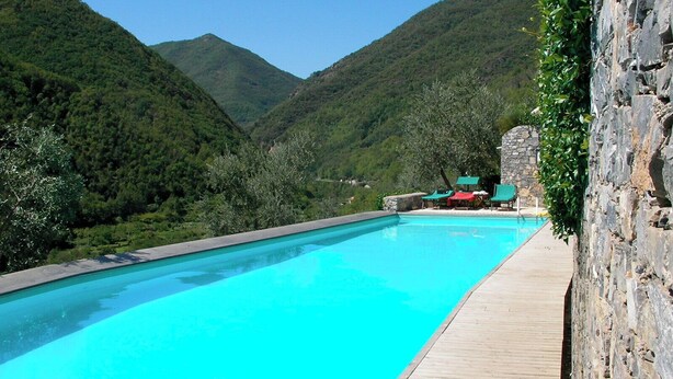 Una piscina con un pontile in legno, circondata da dolci colline verdi e un muro in pietra.