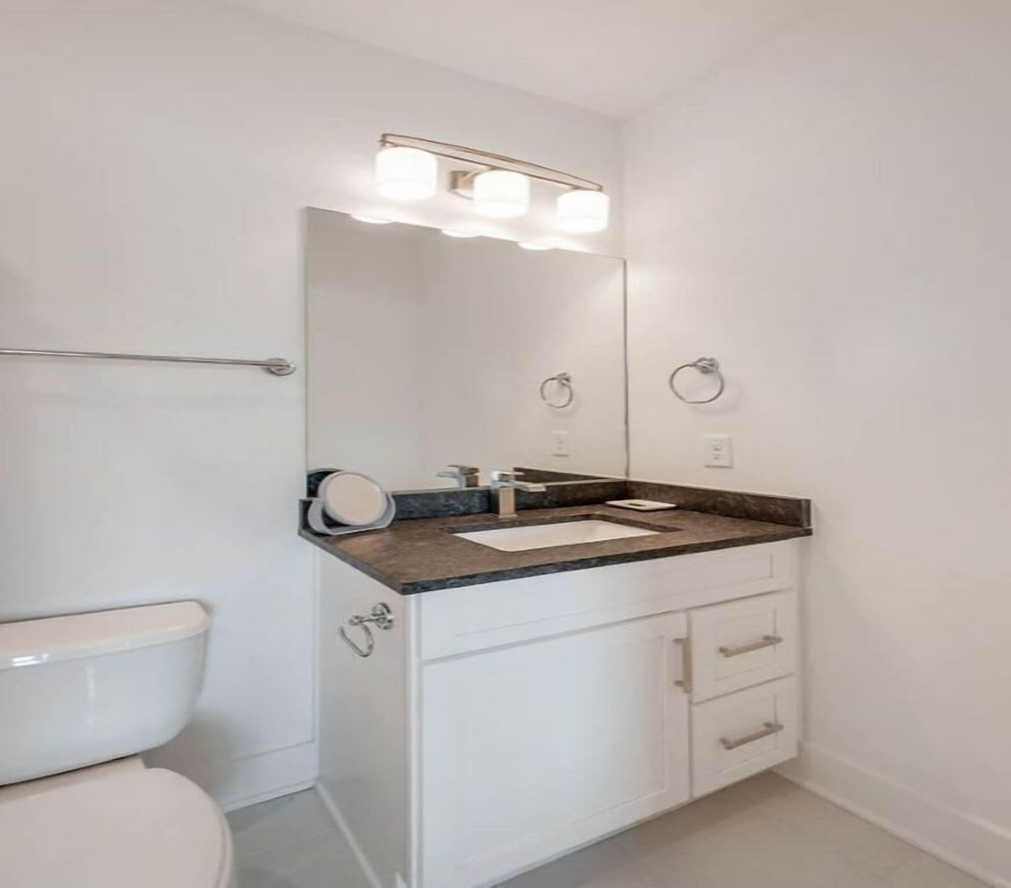 A bathroom with a white toilet, a sink with a mirror above it, and a towel ring on the wall.