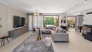 En moderne stue med en grå sofa, et sofabord og et fjernsyn på væggen. Et spiseområde med et bord og stole er synligt gennem den åbne rumindretning.