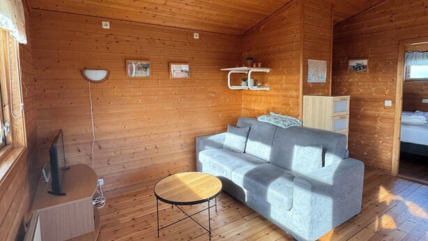 Un interior de cabaña acogedor, con piso de madera, un sofá gris, una mesita redonda y un armario blanco.