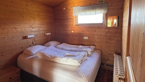 Una habitación de cabaña de madera con una cama, un ventanal con cortina y un radiador.