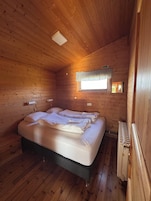 Una habitación de cabaña de madera con una cama, un ventanal con cortina y un radiador.