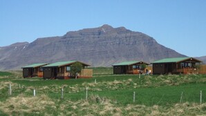 Tres cabañas de madera con techos verdes, ubicadas en un campo cubierto de hierba con una montaña al fondo.