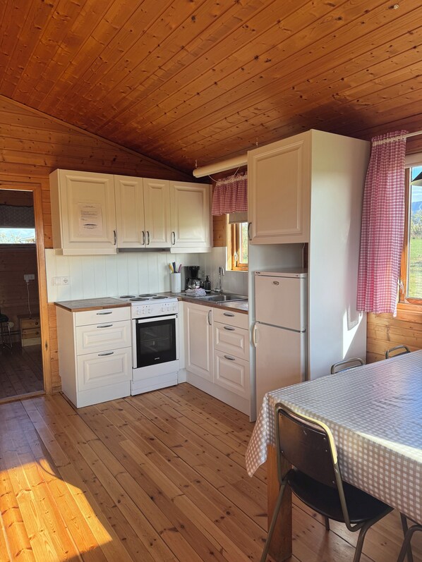 A compact kitchen with wooden cabinets, a stove, and a refrigerator. - Eldborg Cabins & Guesthouse (Borgarbyggd)
