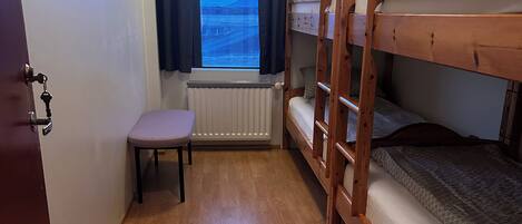 A compact room with a bunk bed, a small table, and a window with curtains.