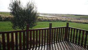 Una terraza de madera con vistas a un campo cubierto de césped y un árbol.