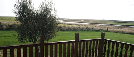 A wooden deck with a view of a grassy field and a tree.