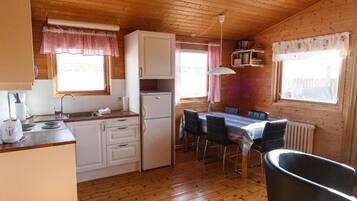 Una cabana de fusta amb zona de cuina, taula i cadira.