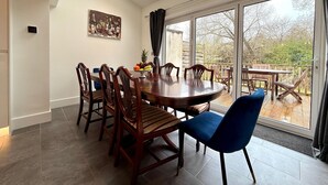 A dining area with a round table, six wooden chairs, and a blue upholstered chair. A fruit bowl is on the table, and there is a painting on the wall. - CosyRiverside House: Contractors, tourists free parking (Hemel Hempstead)
