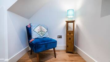 A corner room with a blue chair, a wooden cabinet, and a wall-mounted lamp.