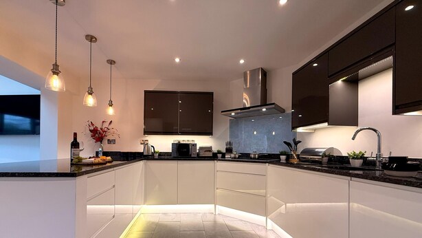 A modern kitchen with a central island, recessed lighting, and a sleek backsplash. - CosyRiverside House: Contractors, tourists free parking (Hemel Hempstead)