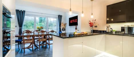 A modern kitchen with a dining area, a large TV screen, and a view of the outdoors.