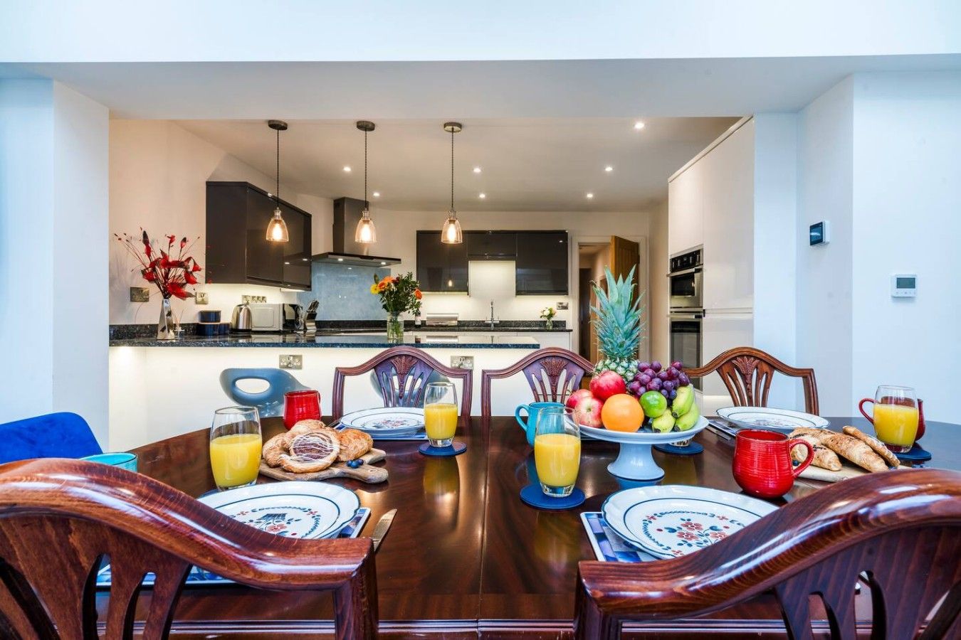 A dining area with a table set for breakfast, including fruits, pastries, and beverages.