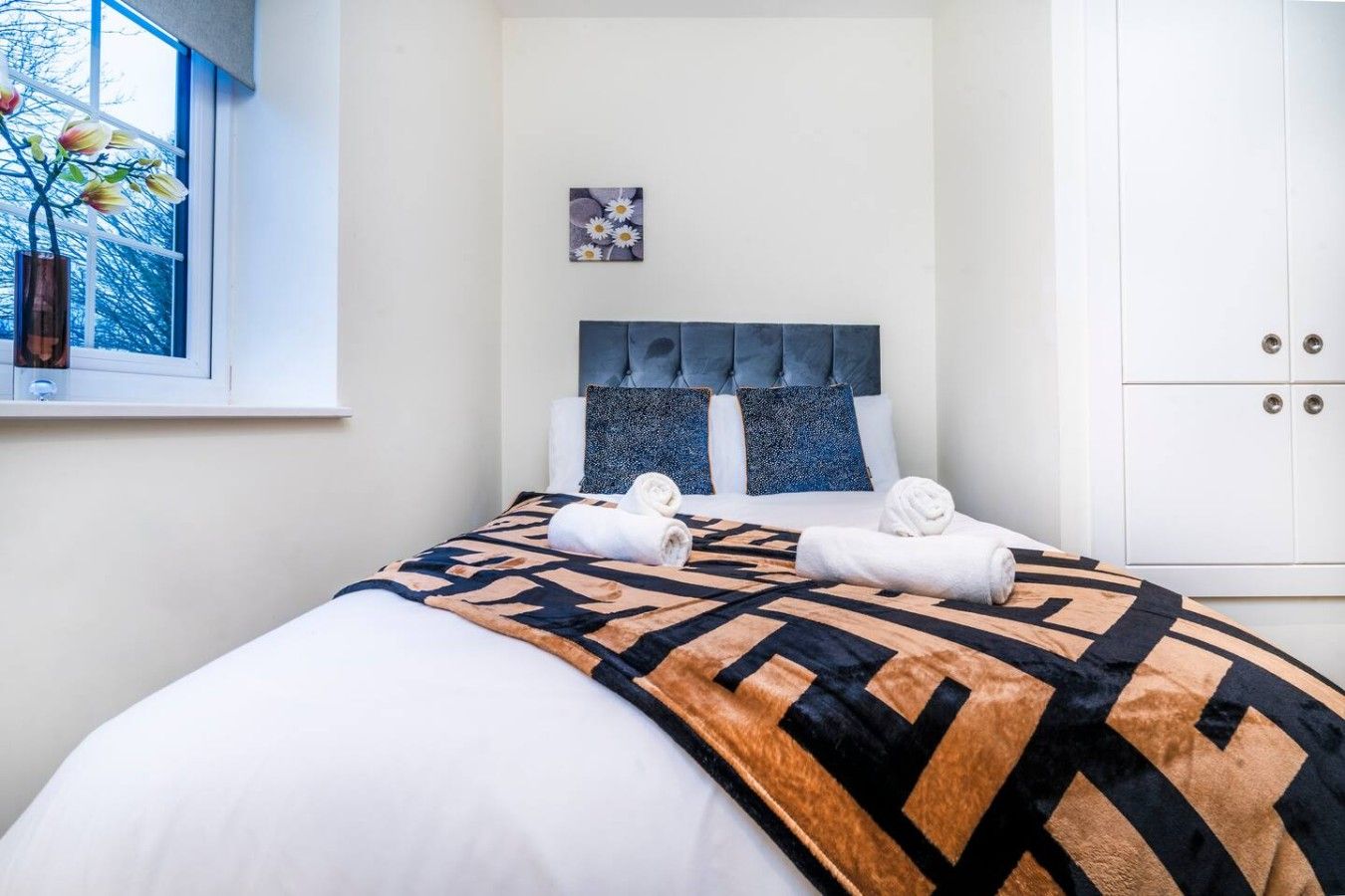 A hotel room with a bed, a window with a view of trees, a painting on the wall, and a wardrobe.