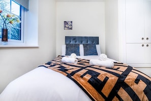 A hotel room with a bed, a window with a view of trees, a painting on the wall, and a wardrobe.