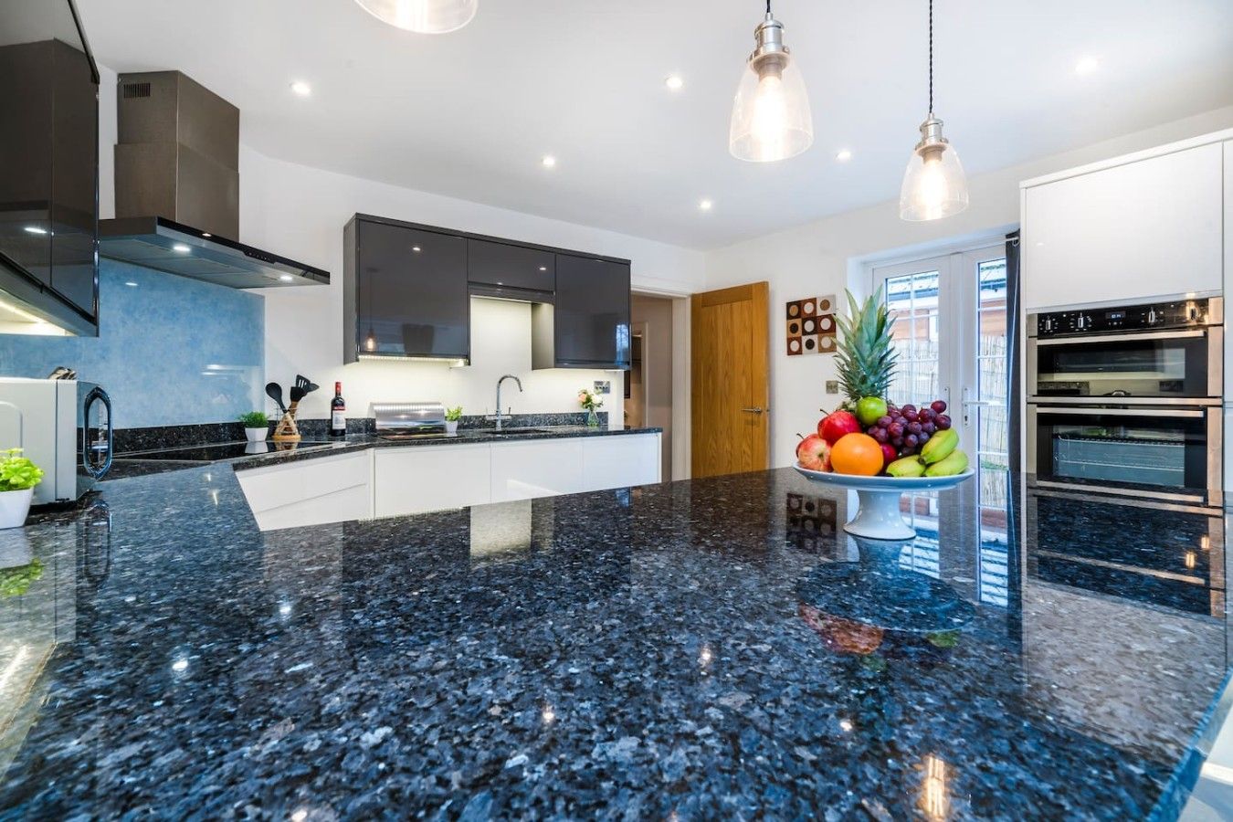 A modern kitchen with a black granite countertop, stainless steel appliances, and pendant lighting.