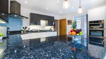 A modern kitchen with a black granite countertop, stainless steel appliances, and pendant lighting.