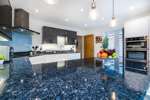 A modern kitchen with a black granite countertop, stainless steel appliances, and pendant lighting.