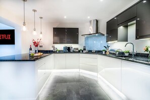 Une cuisine moderne dotée d’un îlot central, d’appareils électroménagers intégrés et de luminaires suspendus.