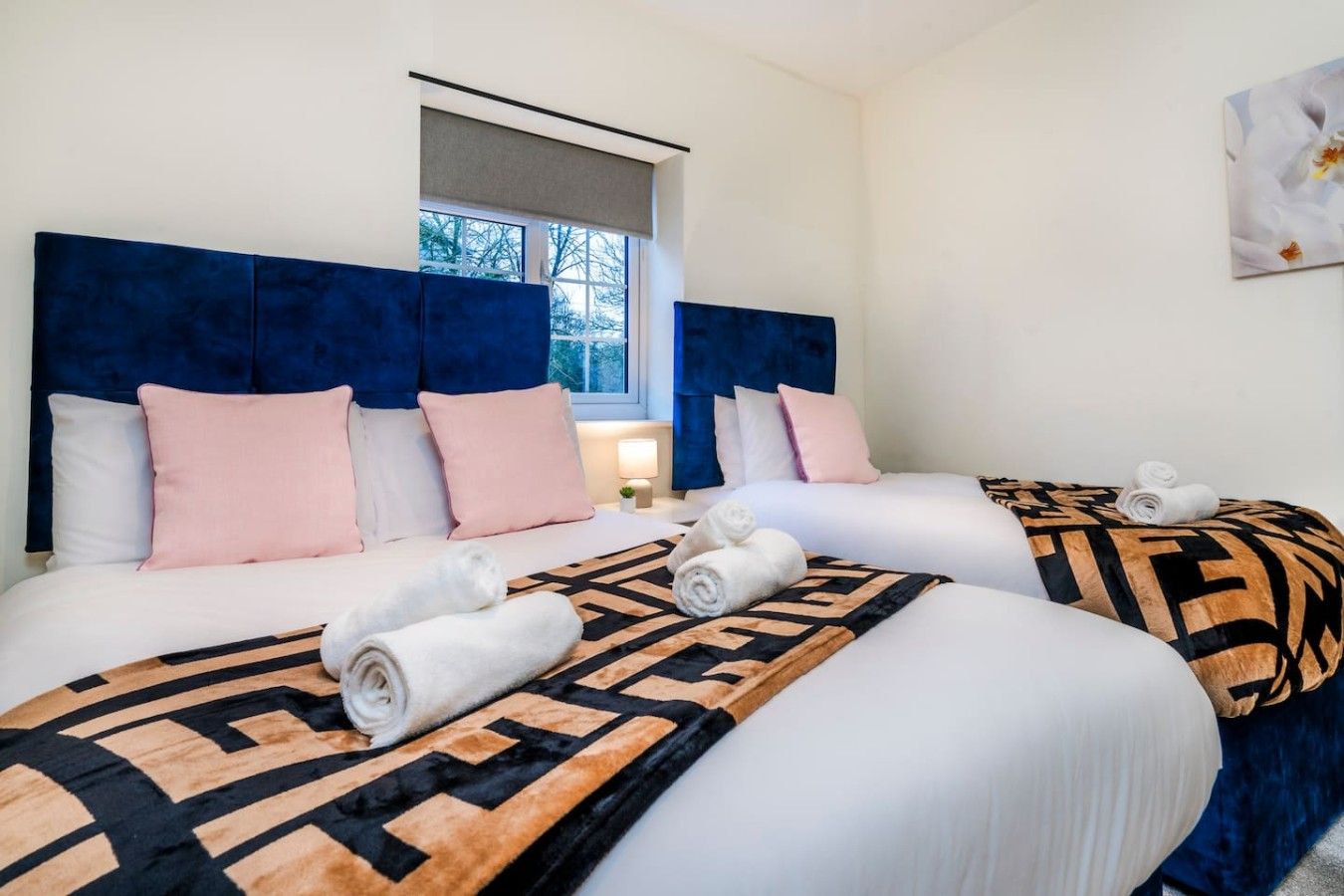 A hotel room with two beds, each with a headboard, pillows, and rolled towels.