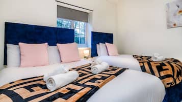 A hotel room with two beds, each with a headboard, pillows, and rolled towels.