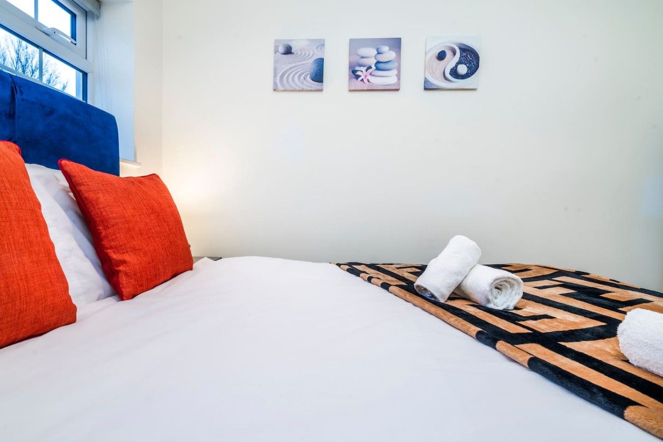 A hotel room with a bed, pillows, a rolled towel, and three wall art pieces.