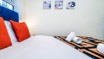 A hotel room with a bed, pillows, a rolled towel, and three wall art pieces.